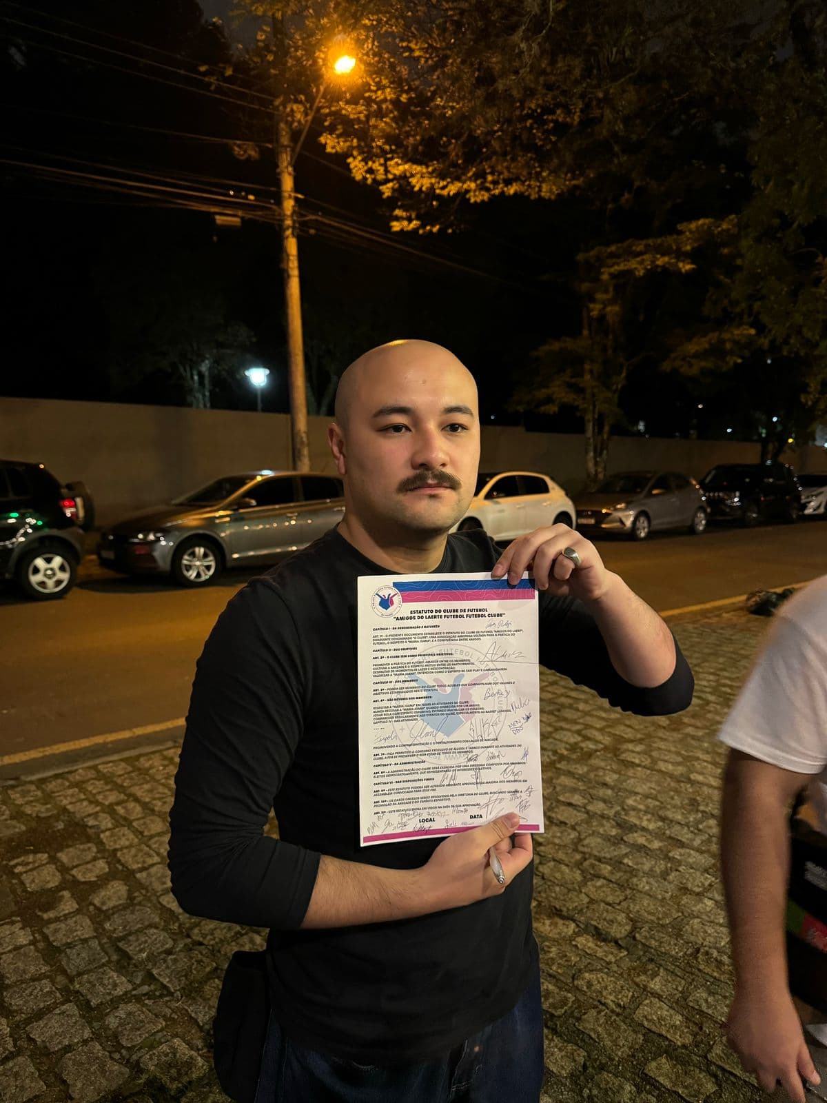 Sócio exibe o estatuto do clube assinado, à noite, na calçada