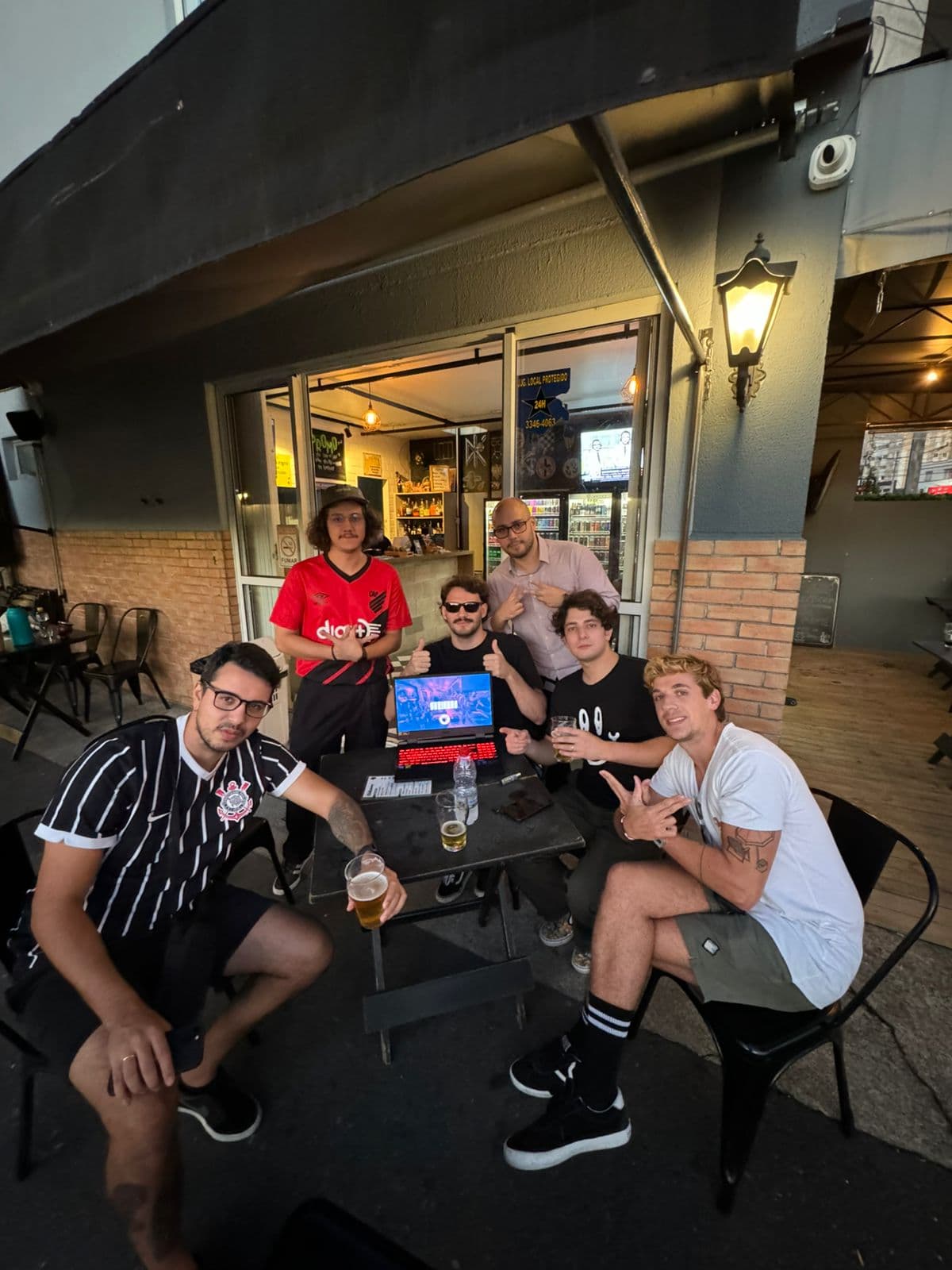 Sócios reunidos na mesa do bar, entre copos e um notebook